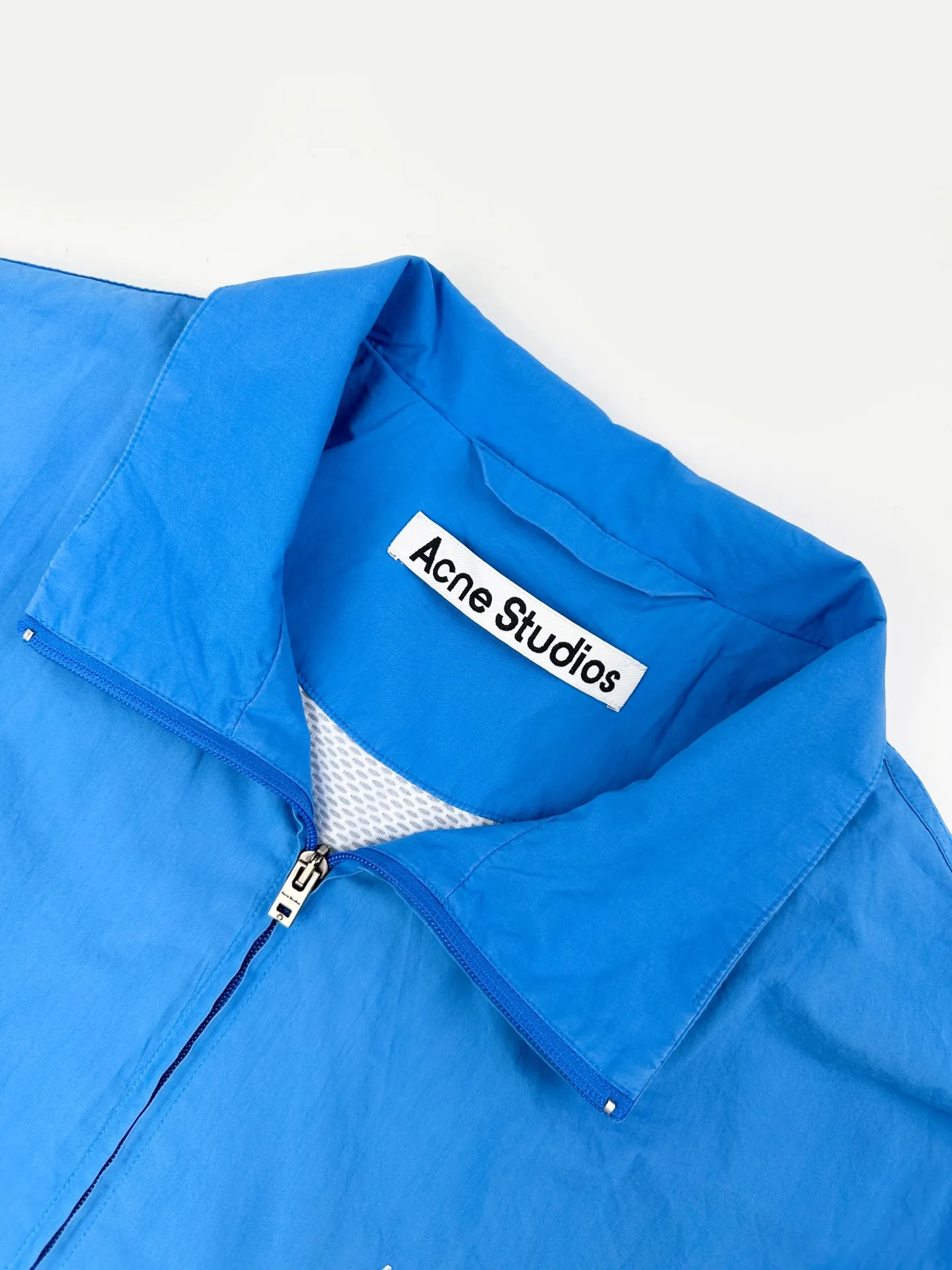 Acnee Studios contrasting logo zipper jacket, custom-made dusty royal poplin, lightweight and crisp, dry and wind-resistant, sophisticated Royal Blue halo body, washed mist to soften the bright tones, interpreting the cool and relaxed luxury unique to Scandinavia, stand-up collar fully zipped coach jacket, cuffs hem elastically gathered, creating a relaxed, drop-top short silhouette, fully lined inside, smooth and neat upper body The Acne Studios print is discreetly engraved on the chest, retaining the brand gene in a restrained and subtle manner. The contrasting Acne Studios Retro emblem is laid out on the back of the garment. One simple and one complex form a clever visual contrast, which reflects the brand's heritage and traces back to the origin of the brand. It uses the Nordic minimalist high-end ready-to-wear language to describe the narrative of relaxed and restrained luxury and elegance. Process 1: Adopt glue printing process. The printing has been revised three times with the film screen. Use glue liquid paint to print the pattern on the fabric. Bake the fabric to fix the printed pattern. Process 2: Gradient distressed spray process. By spraying dyes of different colors on the surface of the fabric, the clothes can show rich color changes under different lights and increase the visual layering. Process 3: Heavy fermentation washing uses a special solution to remove stains and slight fading, and then snowflake washing. Use strong washing to fade the color to make the color more uniform. Process 4: The hem is made in one go using a three-needle waist-drawing machine. The elastic band and the fabric are sewn together in the same process using the special needle position and feeding mechanism of the machine. The three-needle design is more secure and can distribute pressure evenly to ensure that the elastic band and the fabric are tightly fitted. Accessories: Customized 1:1 Acne zipper Customized 1:1 Acne trademark Version: Loose version Size: 42 44 46 48 Style number: 25254